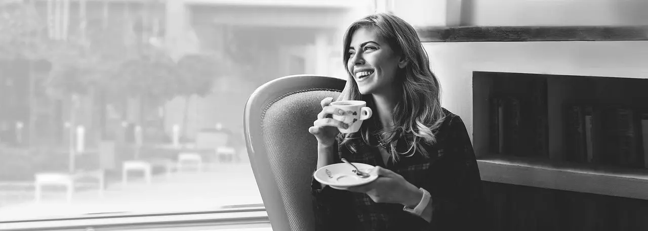 Smilende kvinde med kop kaffe ved vindue